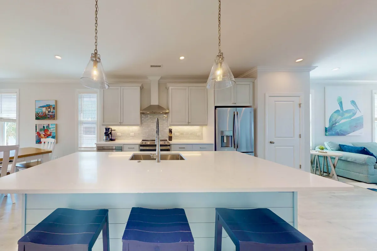 A bright, central kitchen featuring a spacious island with blue bar stools, stainless steel appliances, and inviting artwork on the walls. The layout encourages group cooking and socializing, making it perfect for both big holiday meals and casual coffee mornings.
