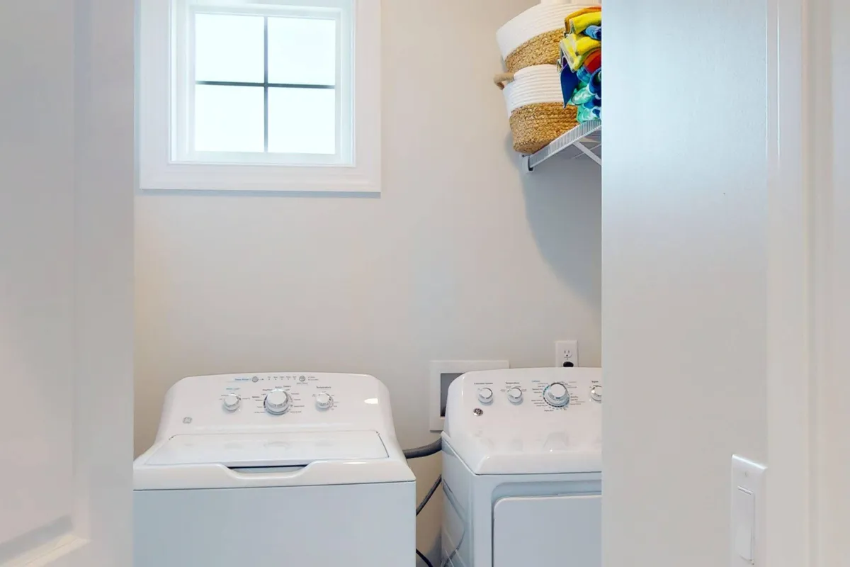A bright laundry room with a washing machine, drying machine, and a window. The space is clean and functional, emphasizing the convenience of onsite laundry for guests staying longer or needing quick refreshes after beach days.