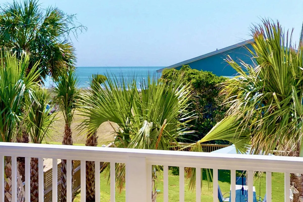 A tranquil exterior scene with palm trees, a lush green lawn, and a broad ocean view. The image suggests a comfortable space for outdoor dining or relaxation, with hints of seating and open space conducive to family gatherings or quiet mornings.