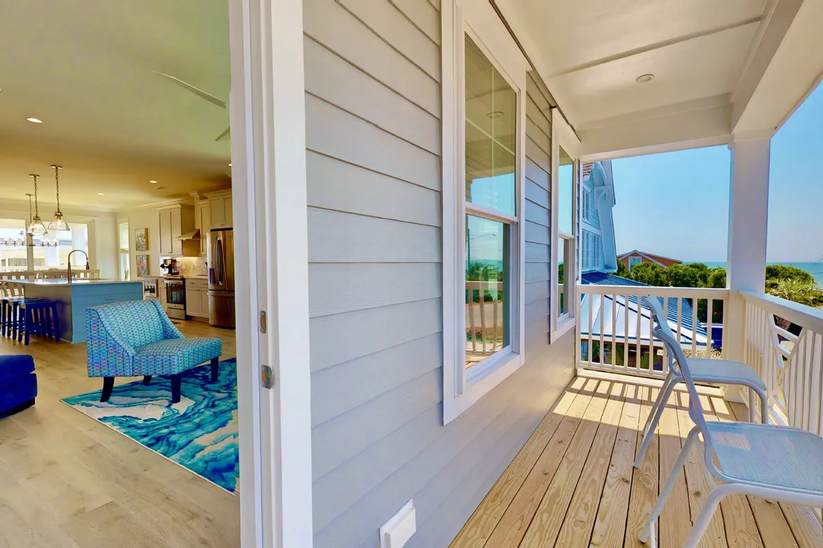 An exterior balcony space with a kitchen area, comfortable chairs, a decorative rug, and scenic views of the landscape. The setup is ideal for grilling, morning coffee, and alfresco dining, extending entertaining possibilities outdoors.