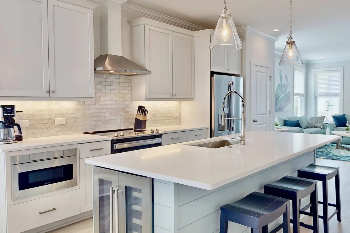 A stylish, modern kitchen with a large island countertop, stainless steel appliances, bar stools, and artisanal backsplash tiles. The open layout invites guests to cook, dine, or chat around the kitchen island.