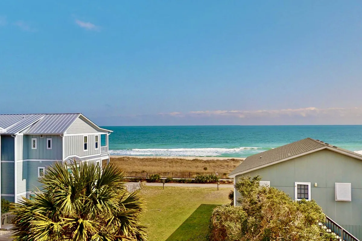 A sweeping view of the ocean framed by palm trees and nearby houses, with space for beach walks, sunbathing, and group picnics. The distant horizon and open sky evoke a sense of retreat and tranquility ideal for gatherings.