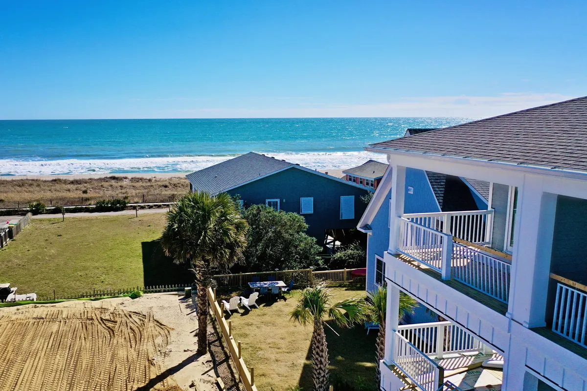 This scenic view looks out over the ocean, with palm trees framing nearby houses and a broad stretch of beach. The tranquil setting suggests relaxation and the enjoyment of nature, with ample space for gatherings, sunbathing, and beach activities.