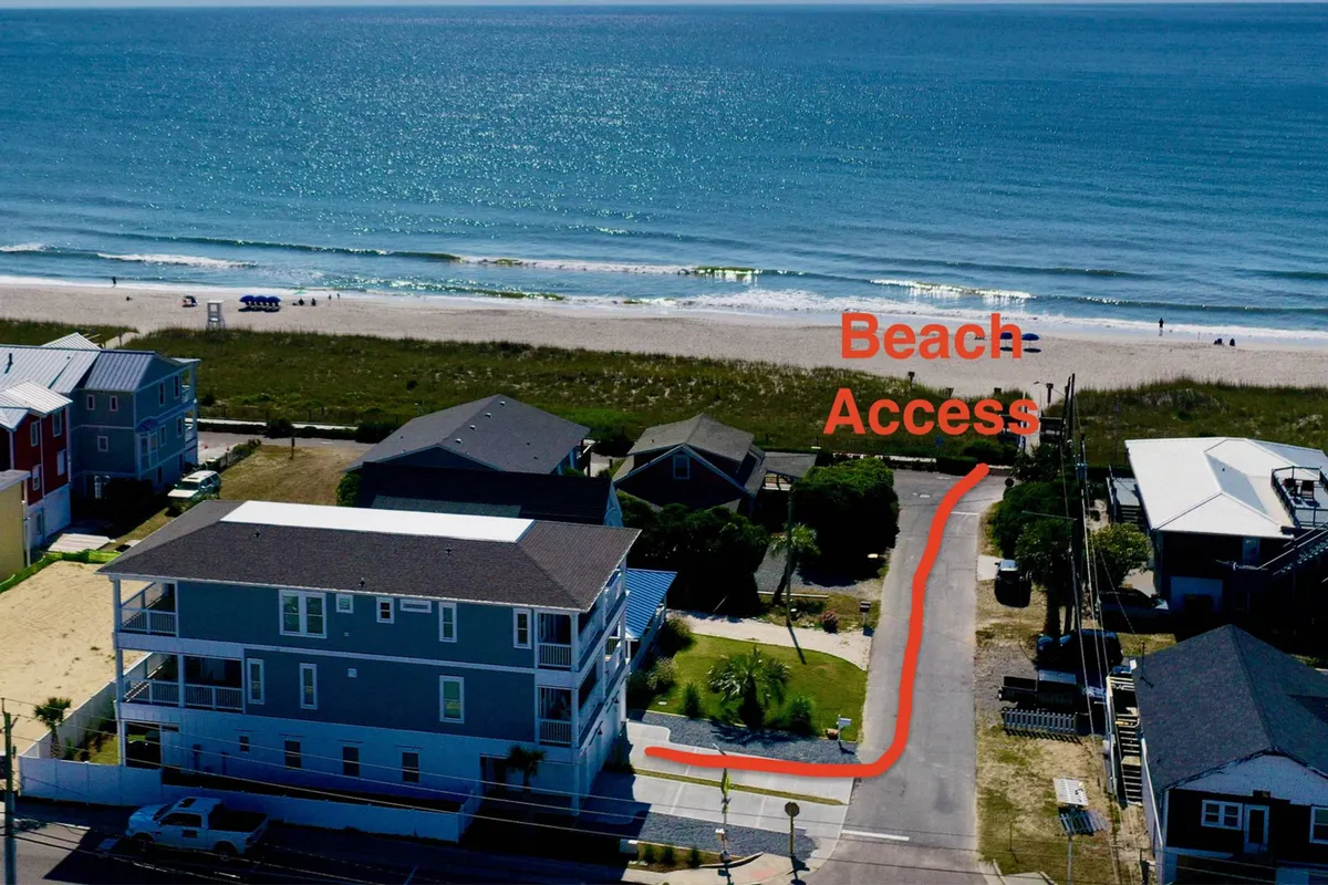 This image features a beach access path leading to the ocean, flanked by nearby houses and bordered by a green lawn. The scene is inviting and tranquil, hinting at easy group access to the beach, with spaces for both activity and relaxation.
