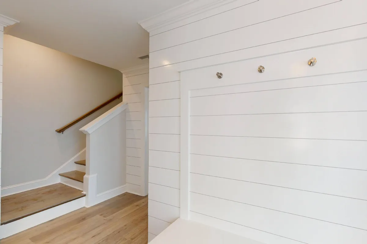 A view of the entryway, featuring a staircase, shiplap wall, and a mudroom bench. The space feels organized and inviting, ideal for dropping beach gear, hanging coats, and making a smooth arrival after time outdoors.