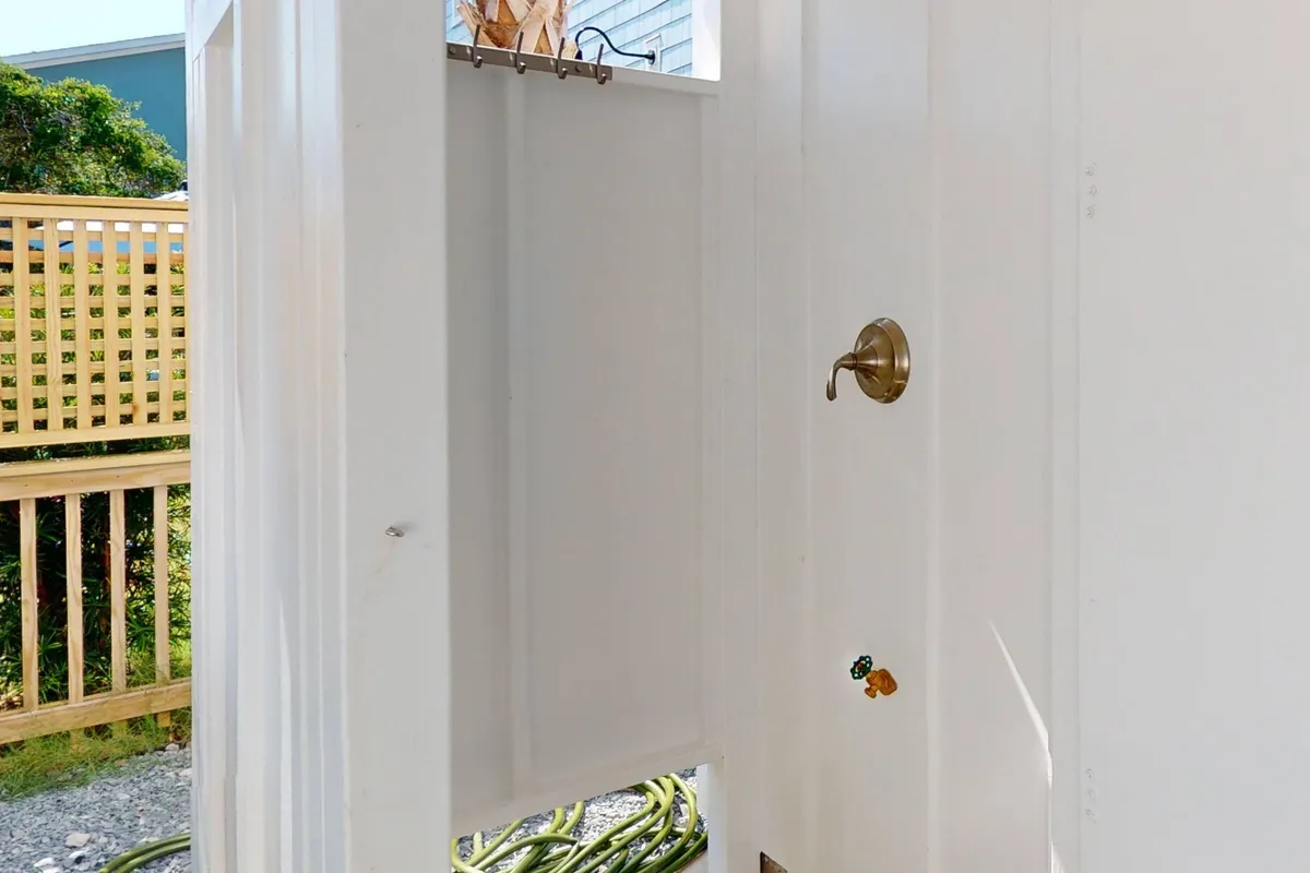 This image shows an outdoor shower with a view through the doorway, evoking a refreshing transition from the sand to the comfort of home. The setup highlights the practical amenity of rinsing off after a day at the beach before heading inside.