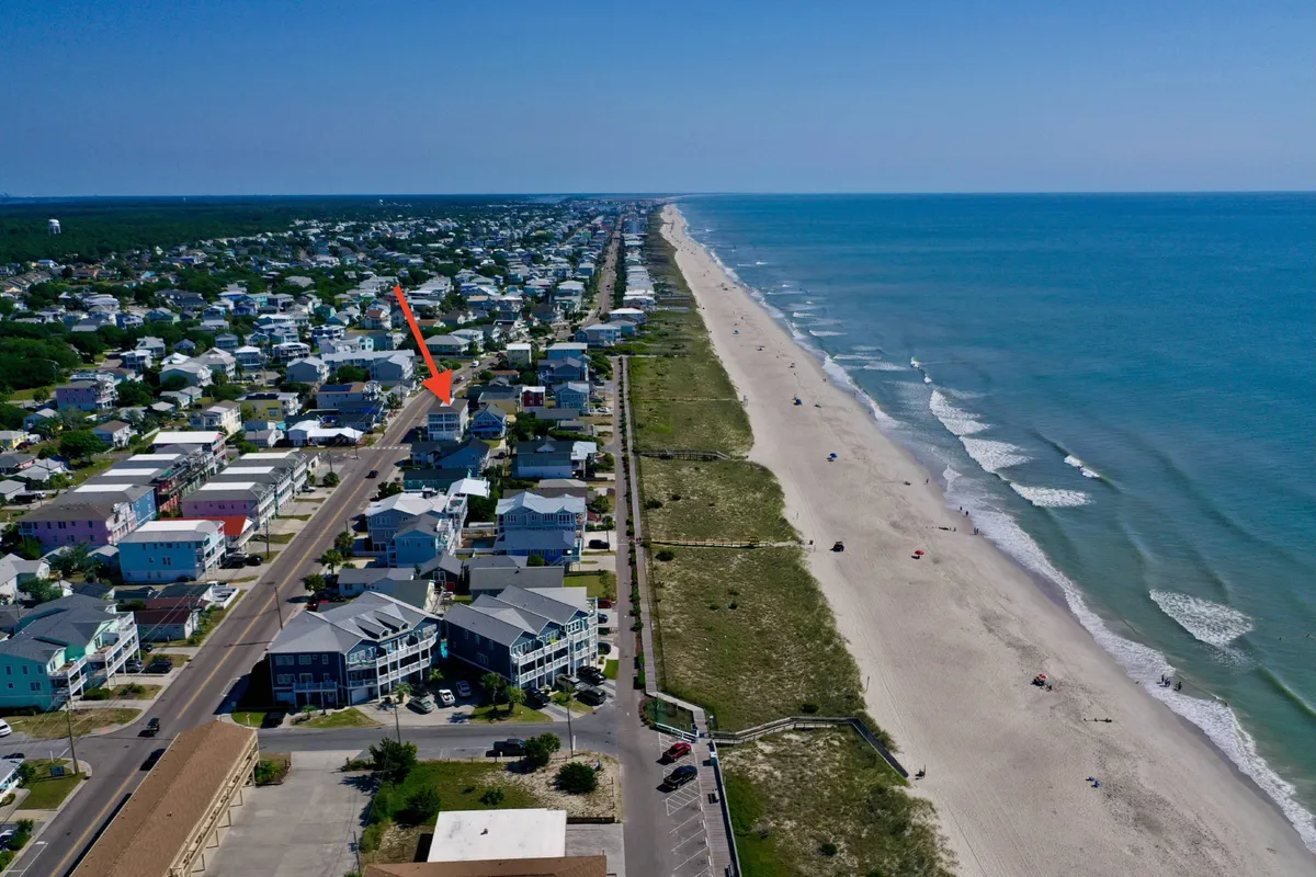 A sweeping view of beachfront properties lining the shoreline, with gentle ocean waves lapping the sand. The area is ideal for water sports, beach walks, sunbathing, and group gatherings, offering a broad perspective of the coastal lifestyle.